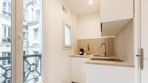 A compact kitchen with a sink, a window, and a view of the street. - Sweett | Madeleine VI (Paris)