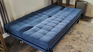A blue sofa bed with dimensions 48" x 78" in a room with a patterned rug and a small wooden cabinet.