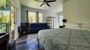A bedroom with a bed, a ceiling fan, a blue sofa, a wooden wardrobe, and a window with curtains.