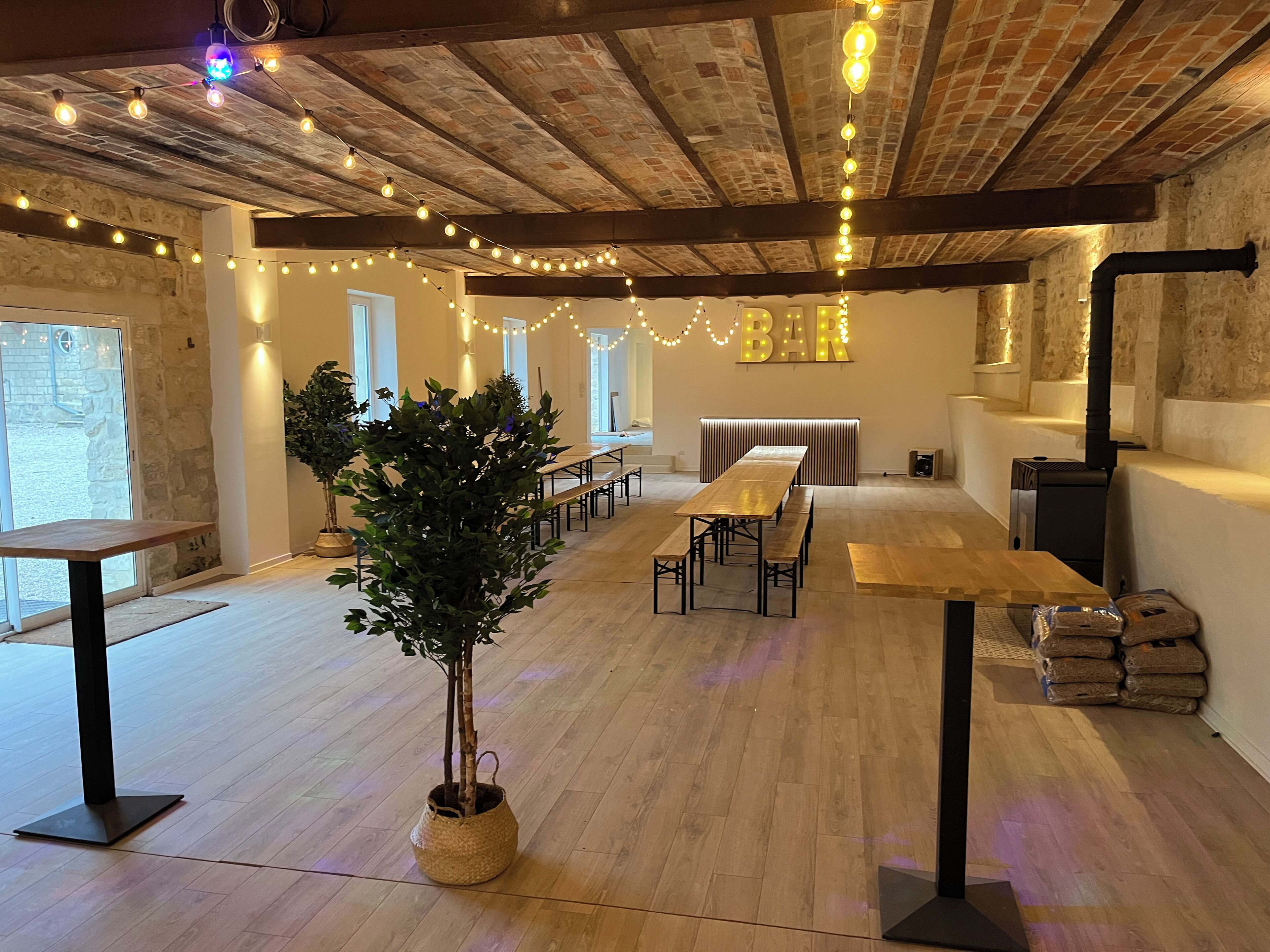 A rustic interior with exposed brick ceilings, wooden tables, benches, and string lights.