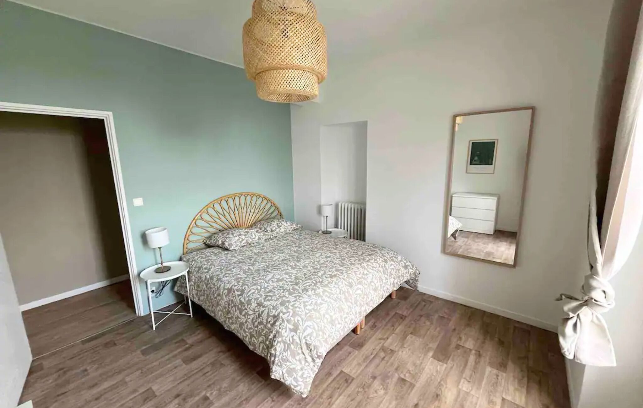 Et soveværelse med seng, et natbord, en lampe, en radiator, et spejl og en pendel.