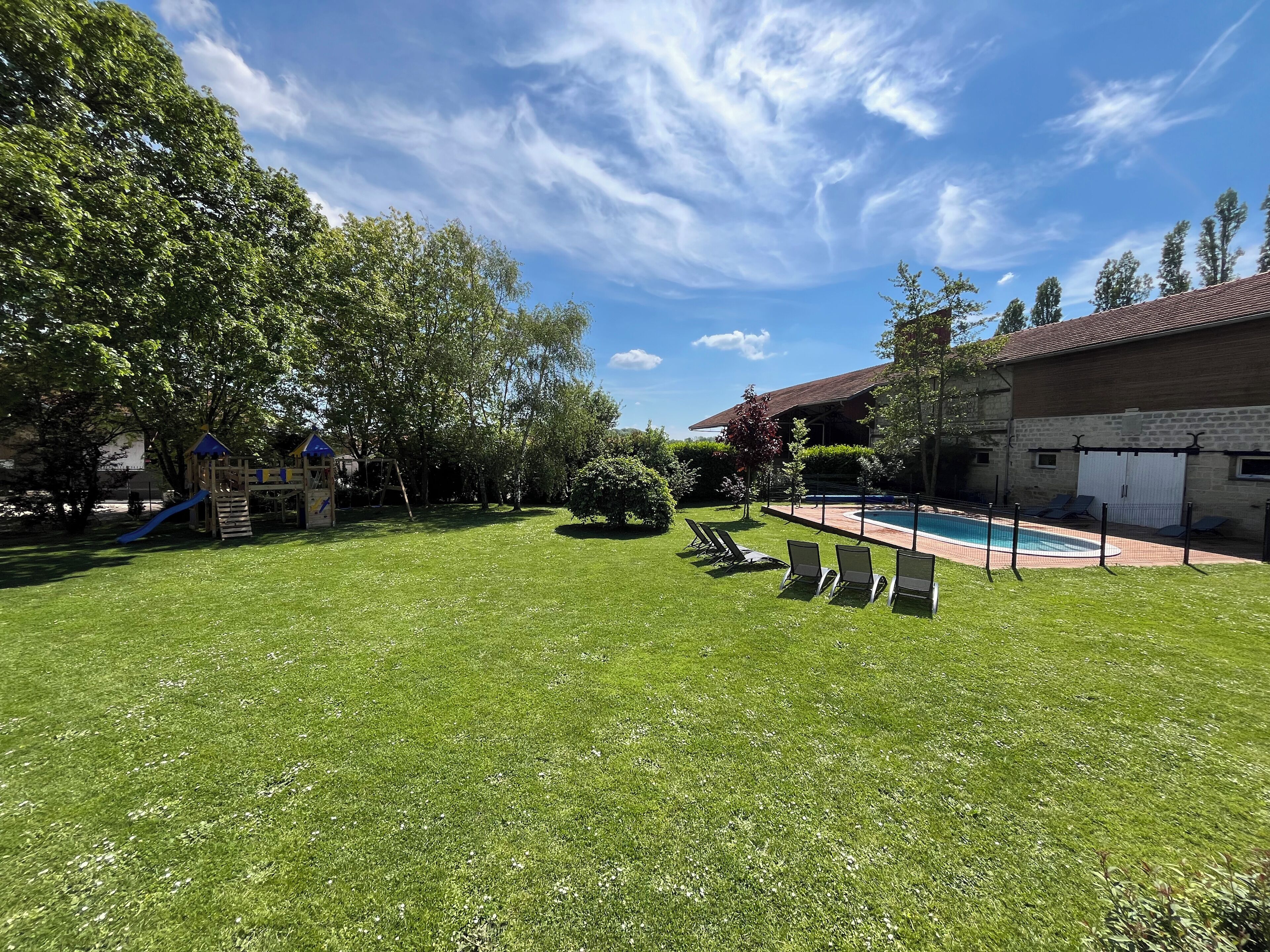 Ett grönområde utomhus med en pool, solstolar och en lekplats.