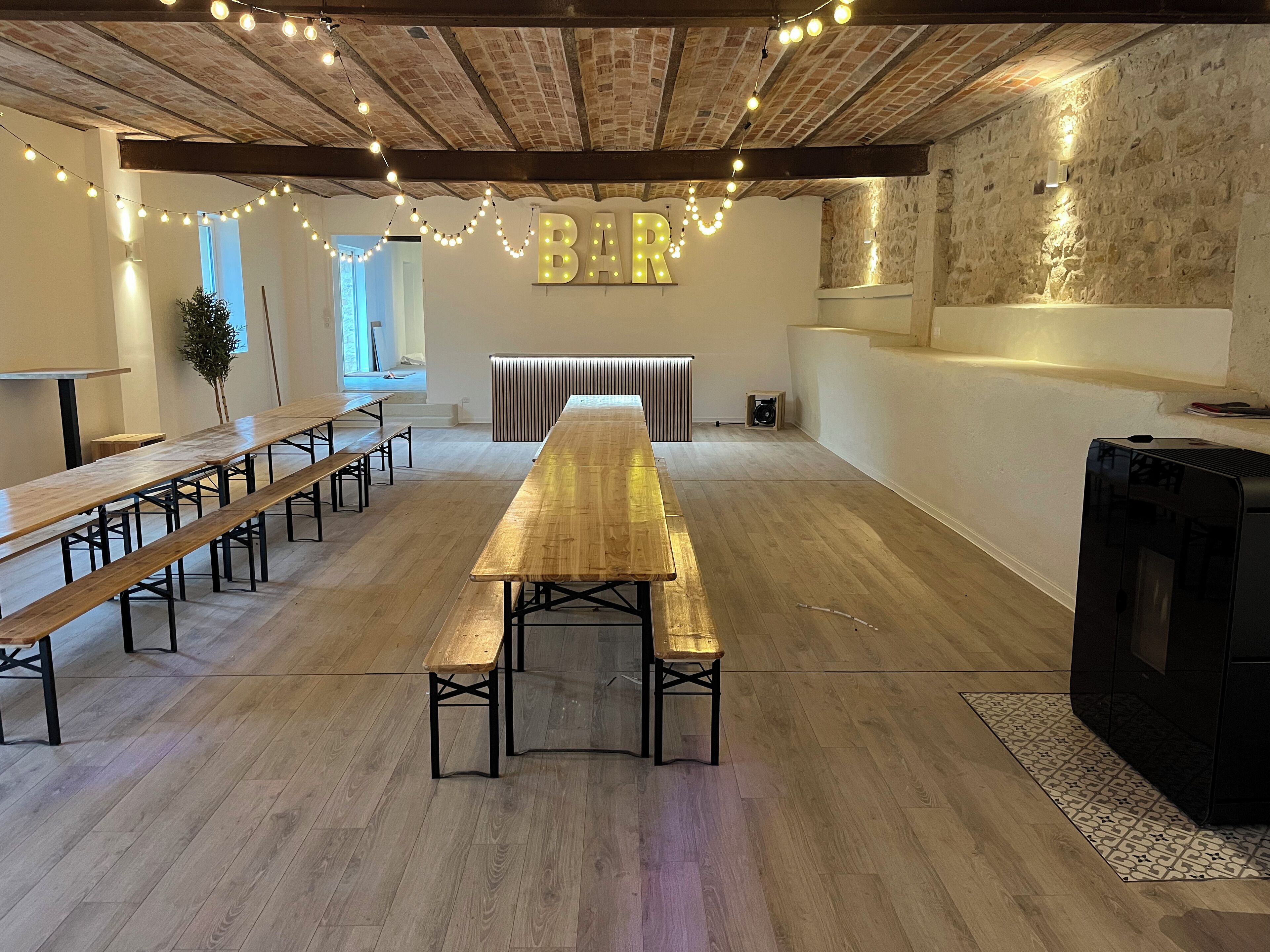 A spacious room with a long wooden table and benches, a stone wall, and a 'BAR' sign.