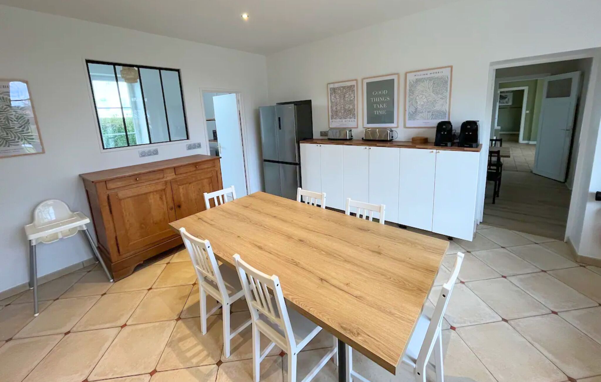 Una cocina moderna con una mesa y sillas de madera, armarios blancos y un refrigerador.