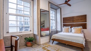 Une chambre avec un grand lit, un miroir, un ventilateur de plafond et une vue par la fenêtre.