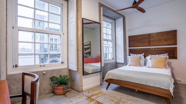 Une chambre avec un grand lit, un miroir, un ventilateur de plafond et une vue par la fenêtre.