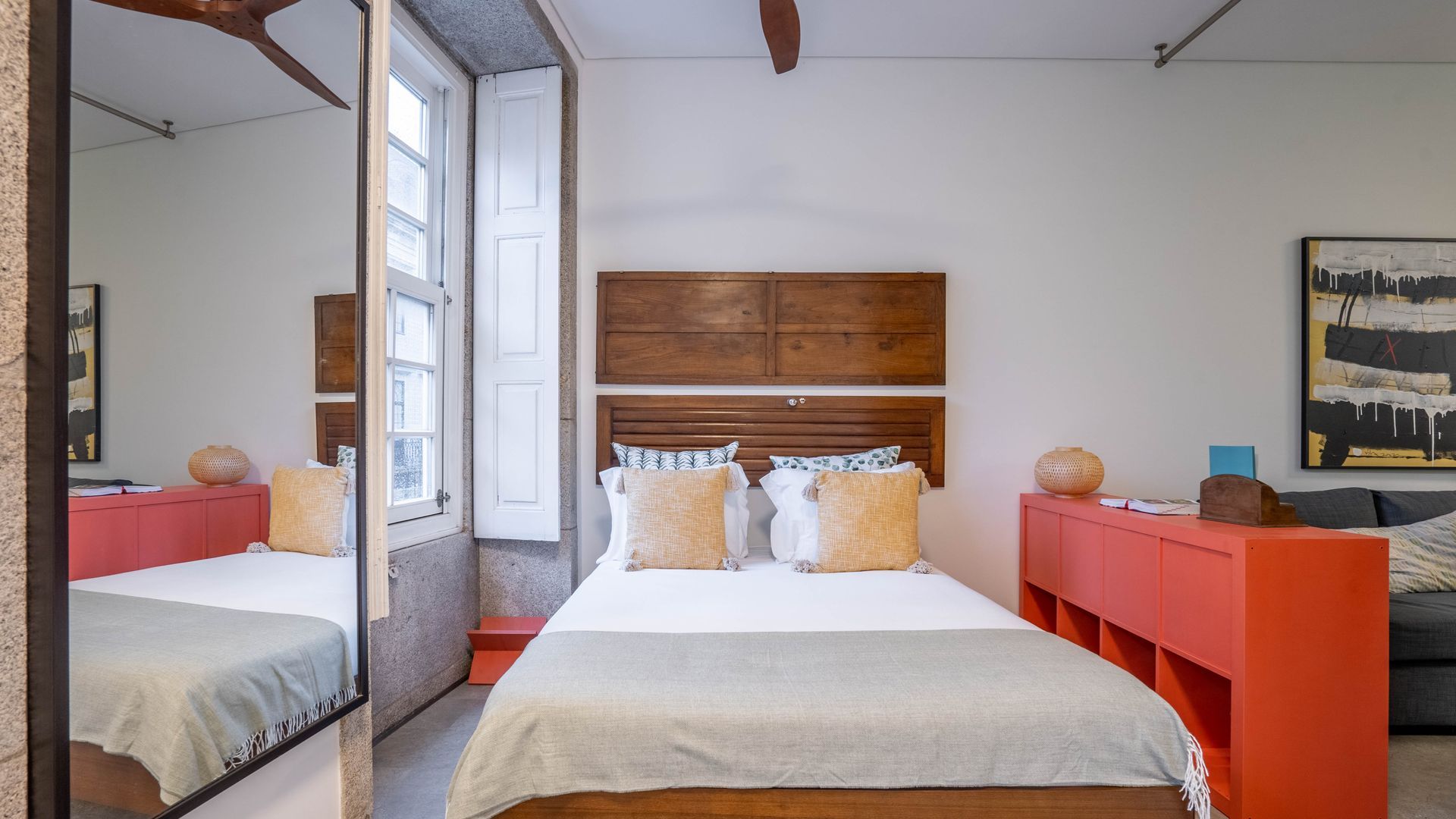 Quarto com cama grande, cabeceira de madeira, armário vermelho e um quadro na parede.