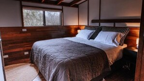 Un dormitorio con cabecera de madera, un ventanal grande y una cama con manta acolchada.
