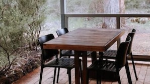 Un espacio de comedor al aire libre techado, con una mesa y sillas de madera, rodeado por un paisaje natural.