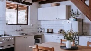 Una cocina con vigas de madera, armarios blancos, una mesa de comedor con sillas y una ventana.