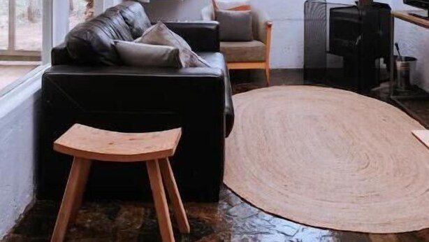 Un salón acogedor con un sofá de cuero negro, un taburete de madera, una alfombra tejida y una chimenea.