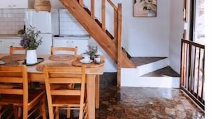 Una escalera de madera lleva a un comedor con una mesa dispuesta para cuatro personas, sobre un suelo de piedra.