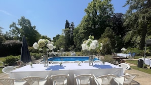 An outdoor dining area with a pool in the background, surrounded by greenery and trees. - Victorian Mannor House with easy London access  (Godalming)