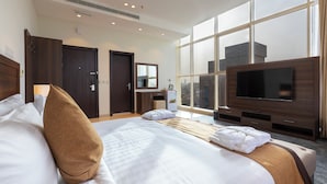 A hotel room with a large bed, a TV, a desk with a chair, and a window with a city view. - Seiba Serviced Apartments- Riyadh (Riyadh)
