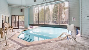 Ein Hallenbad mit Blick auf Bäume durch große Fenster, ein Rettungsschwimmerstuhl und ein Poollifter.
