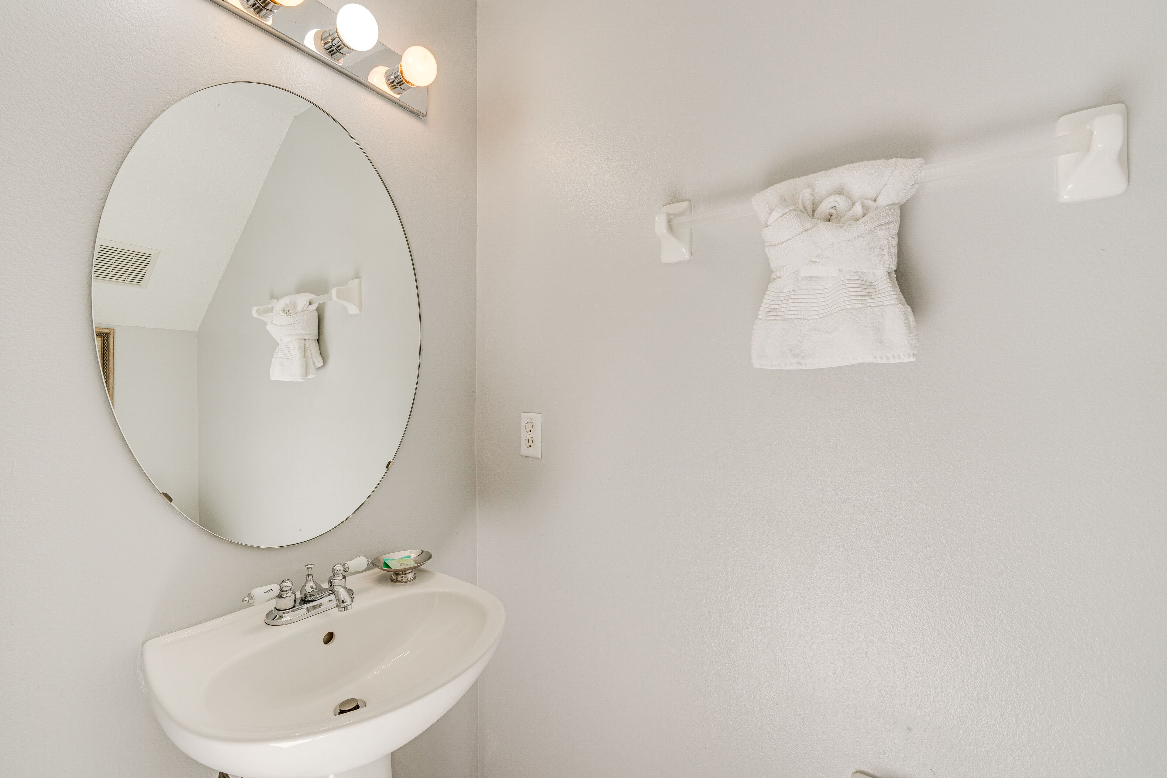 A bathroom with a white sink, a large mirror, and a towel rack with a towel.