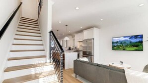 A modern kitchen with white cabinets, a stainless steel refrigerator, and a dining area with a grey sofa and a small round table. - Newly Built 3BR Home in Alexandria-Walk to Metro!

 (Alexandria)