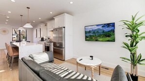 A modern kitchen with white cabinets and stainless steel appliances, a dining area with a sofa and table, and a large painting on the wall. - Newly Built 3BR Home in Alexandria-Walk to Metro!

 (Alexandria)