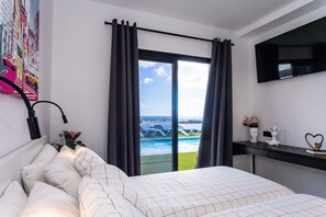 Quarto com cama, escrivaninha, televisão e vista para uma piscina e edifícios.