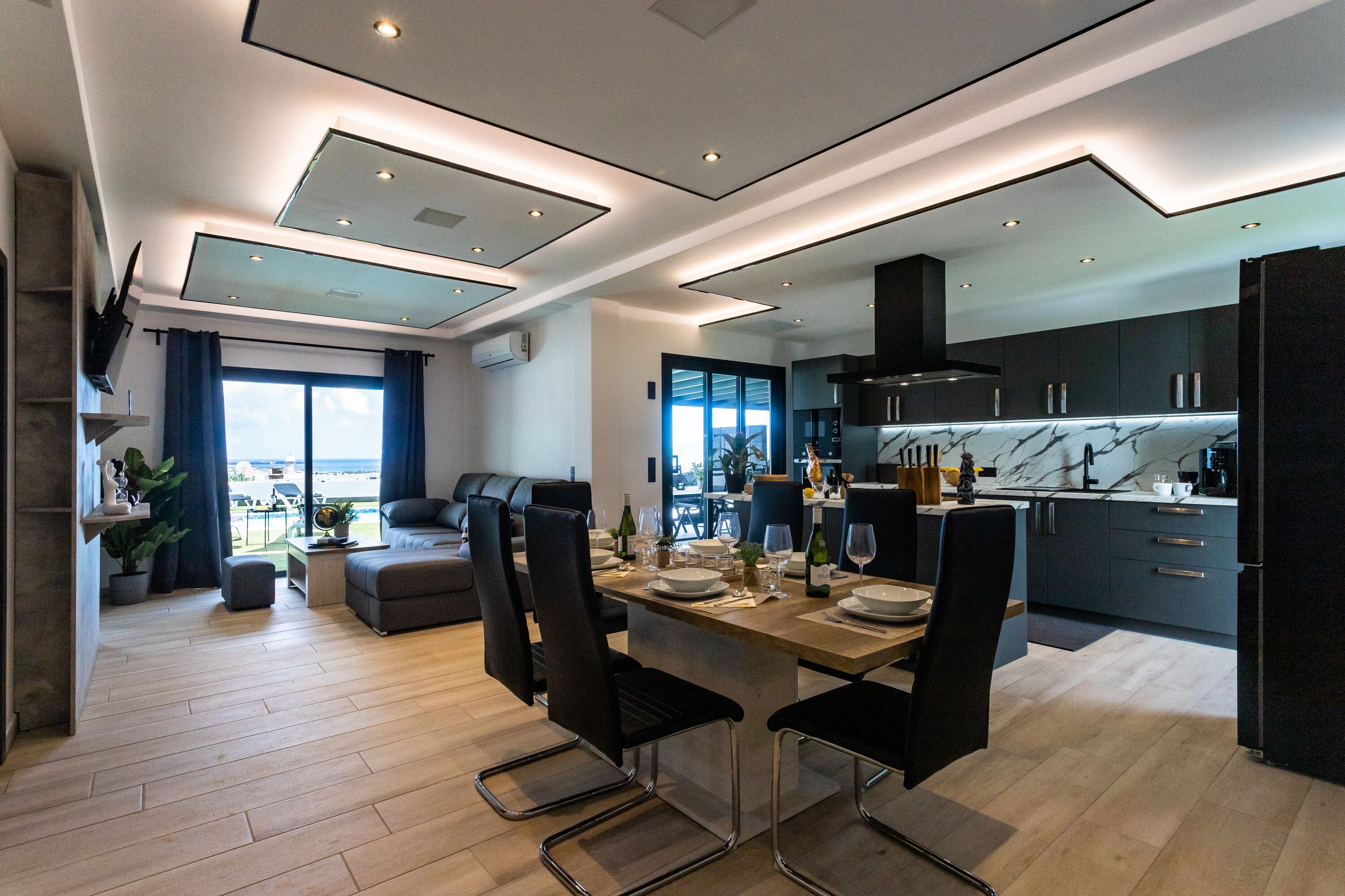 Una cocina moderna con armarios oscuros, un salpicadero de mármol y una zona de comedor con una mesa de madera y sillas negras.