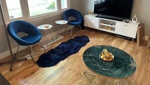 A modern living room with a large flat-screen TV, two blue chairs, a small round table, a dark blue fur rug, and a green marble coffee table. - ALL NEW - Clean & Modern! Mountain Garden Oasis! (Ogden)