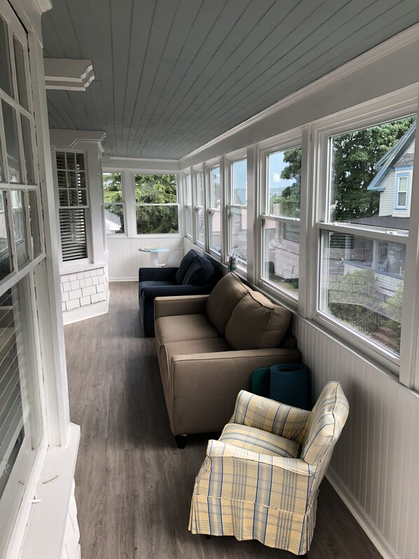 A sunroom with a beige sofa, a plaid armchair, and a view of the neighborhood.