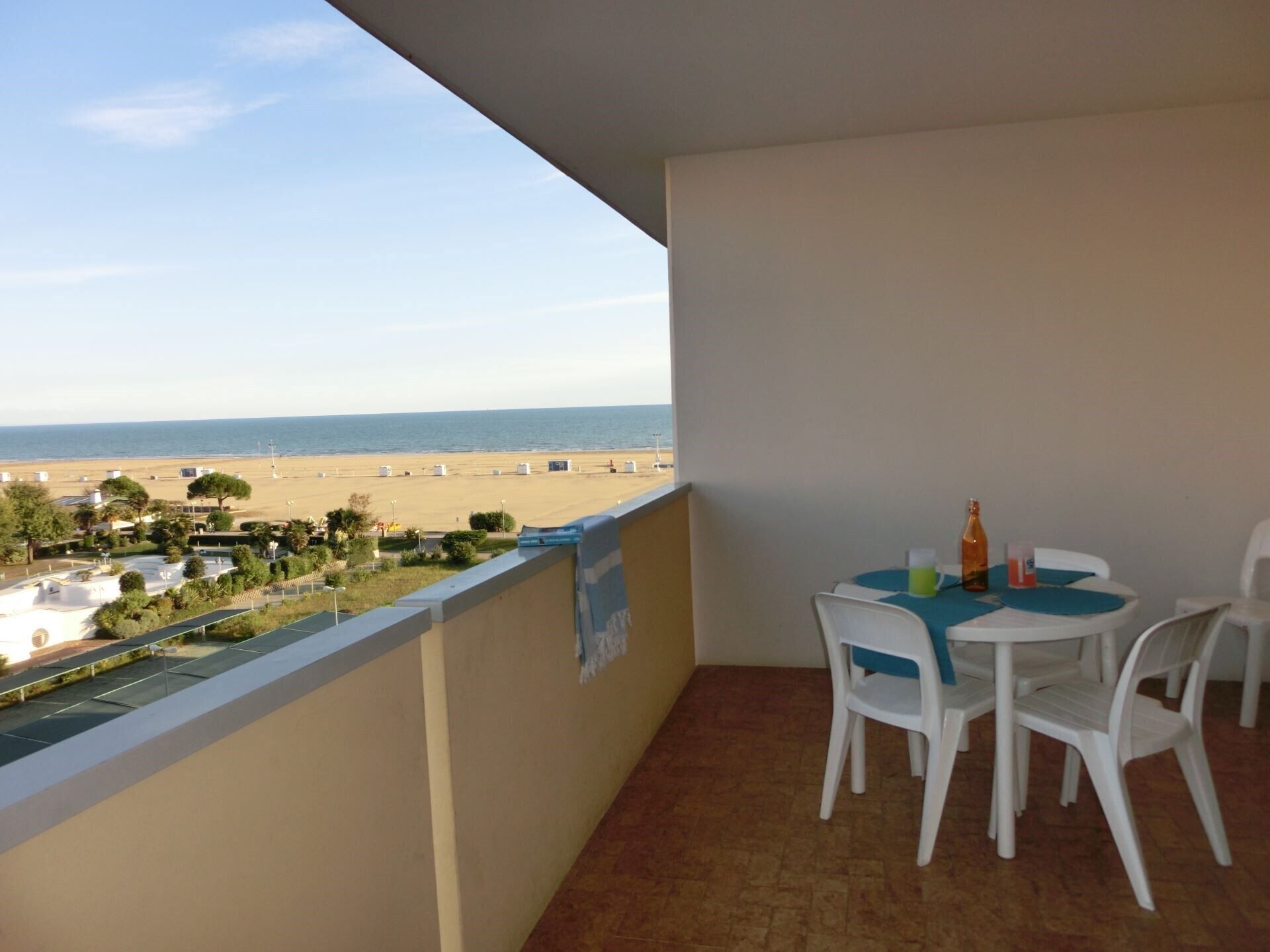Ein Balkon mit Blick auf den Strand, einem Tisch mit Stühlen und einer Flasche.