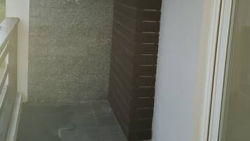 Canto de um quarto com parede de tijolos escuros, parede branca e porta de vidro.