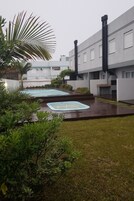 Un patio con dos jacuzzis, rodeado de exuberante vegetación y un edificio moderno con amplios ventanales y una chimenea.