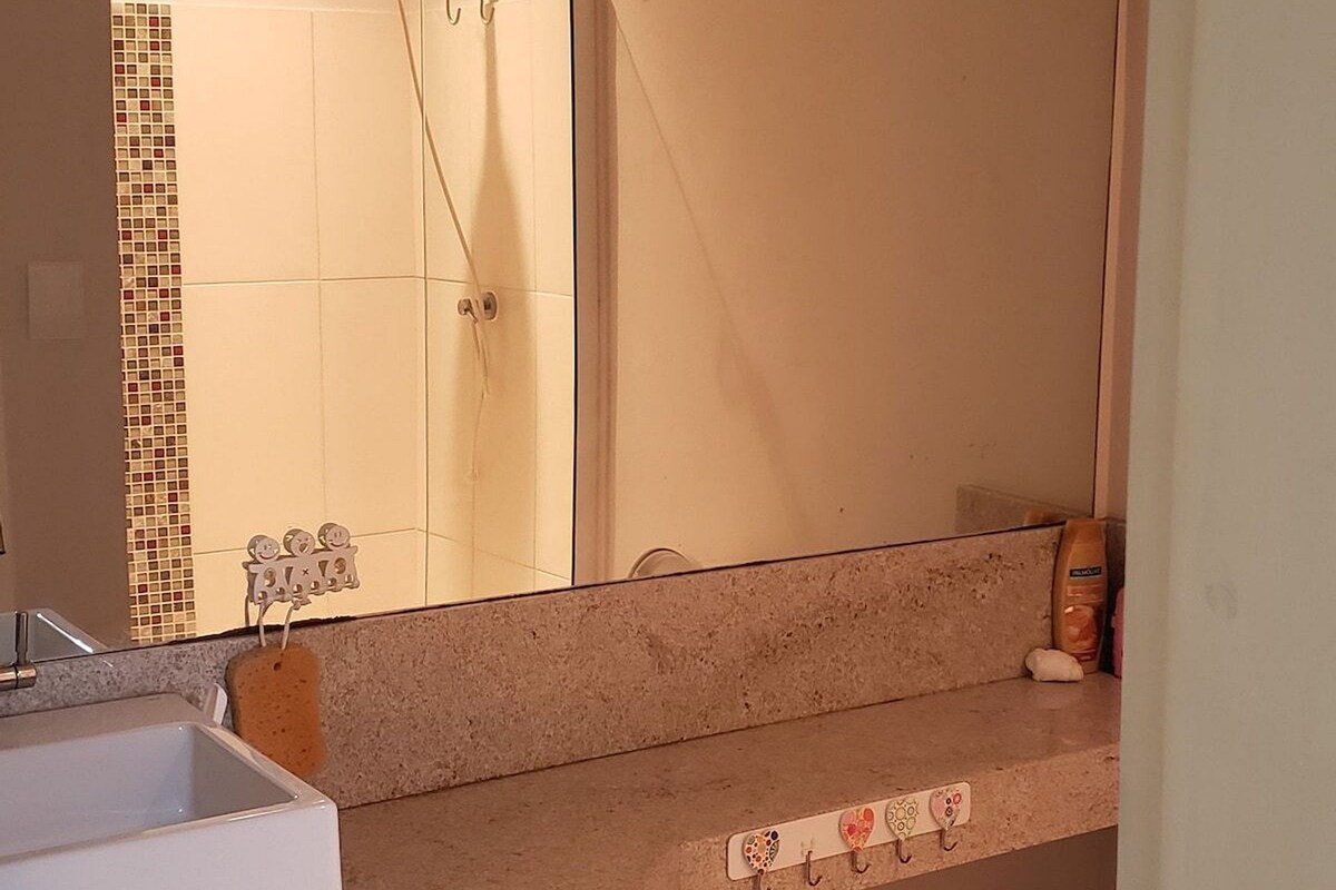 A bathroom with a sink, mirror, shower, and towel rack.