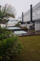 Un patio con dos tinas de hidromasaje, rodeado de follaje y un edificio moderno con amplias ventanas.