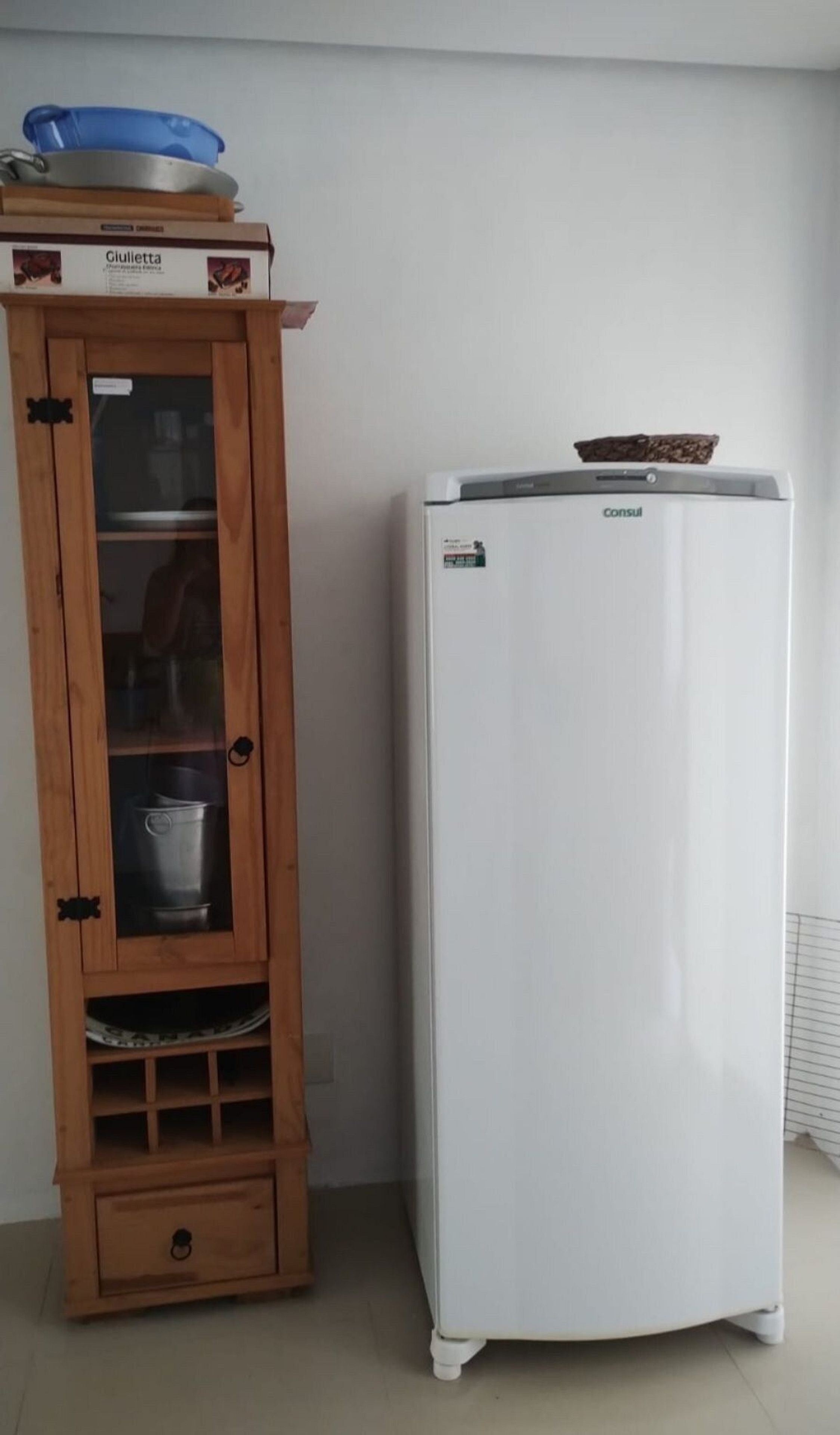 A white refrigerator with a freezer on top, next to a wooden cabinet with a glass door, containing kitchenware.