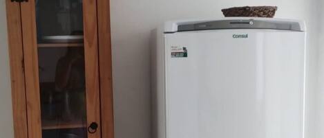 A white refrigerator with a freezer on top, next to a wooden cabinet with a glass door, containing kitchenware.