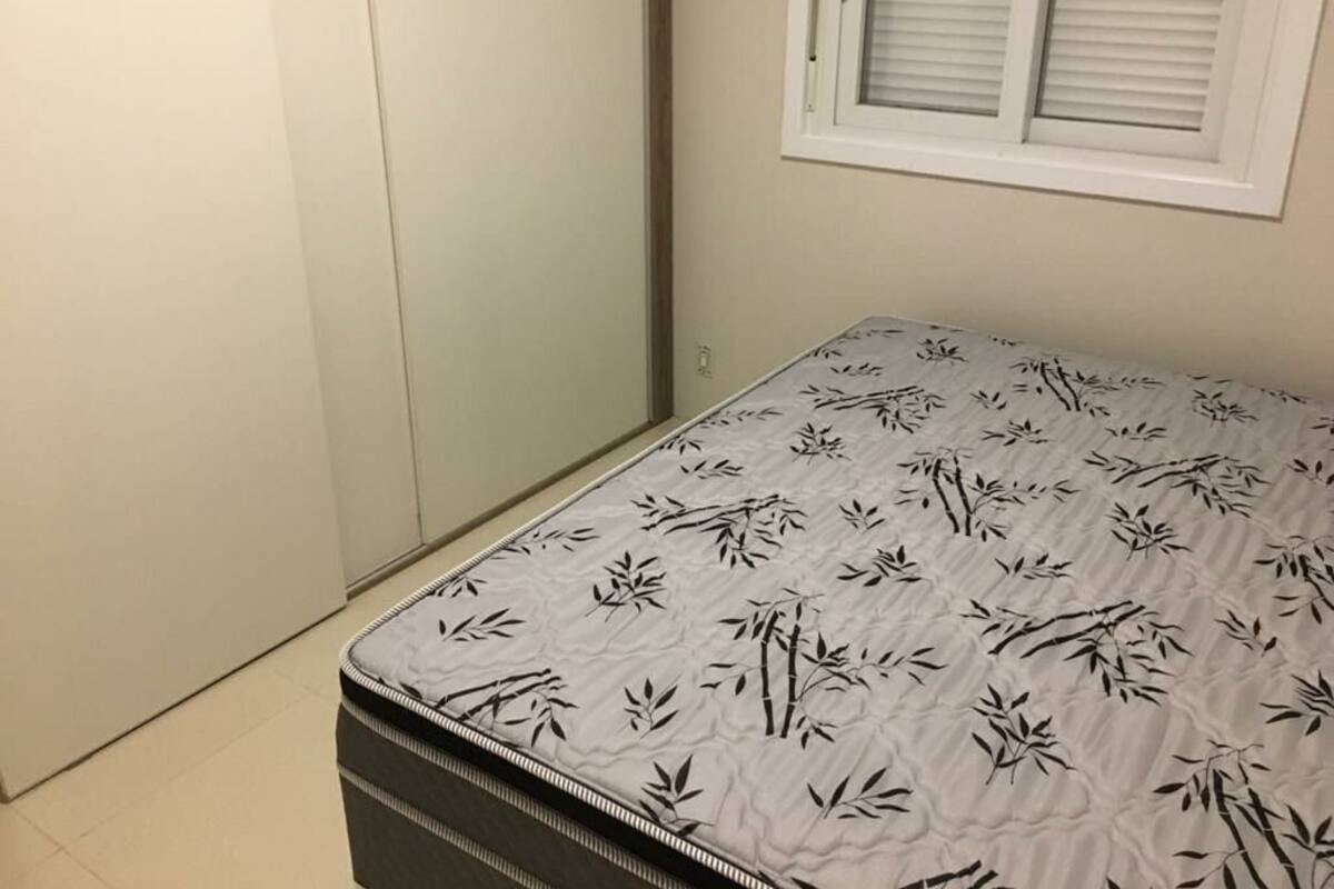 A bedroom with a bed covered in a bamboo-patterned bedspread, a closed wardrobe, and a window with blinds.