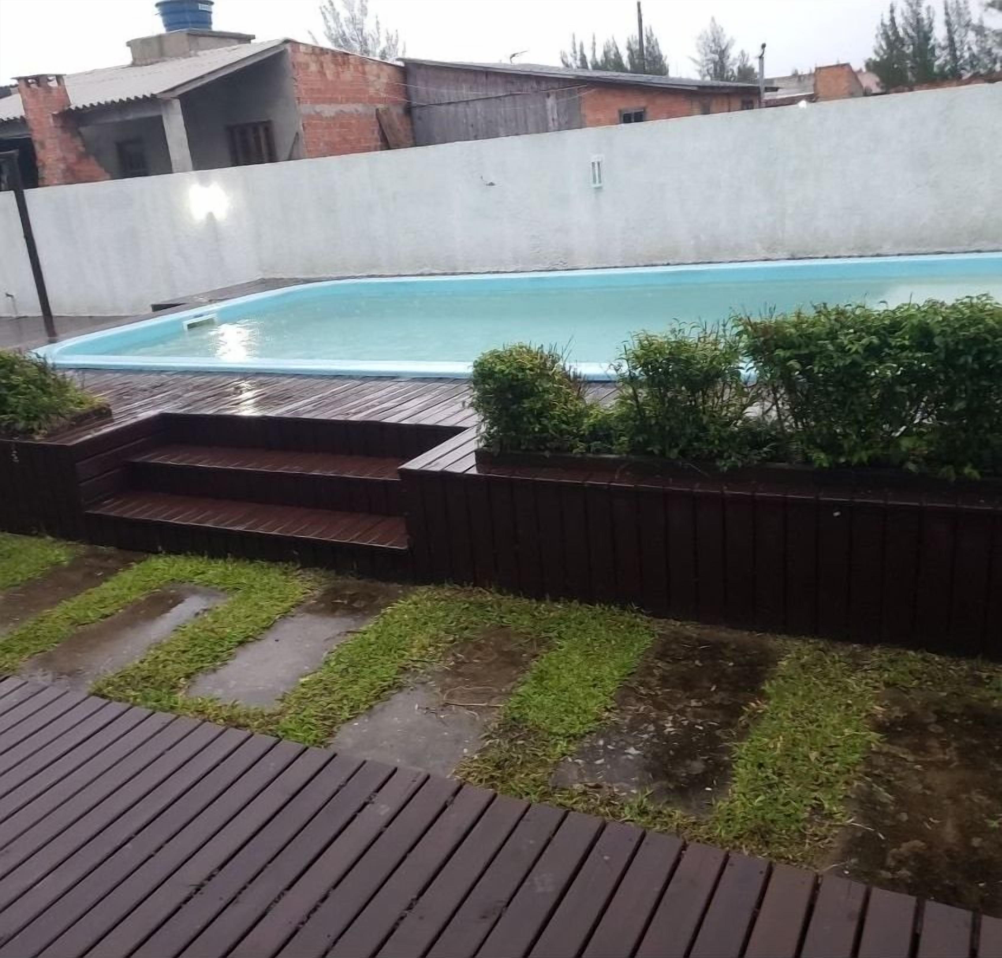 A rectangular swimming pool with a wooden deck and steps leading into it, surrounded by a low brick wall and a hedge.
