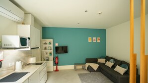 Una sala de estar moderna con una pared de acento color turquesa, un sofá gris y una zona de cocina con microondas y hervidor.