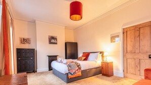 Quarto com cama, mesas de cabeceira, guarda-roupa e luminária pendente vermelha.
