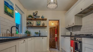 Cozinha com armários brancos, piso de mármore, fogão e luminária pendente.