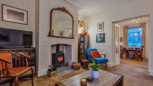 Uma sala de estar com lareira, televisão, área de jantar com mesa e cadeiras, e um espelho grande na parede.