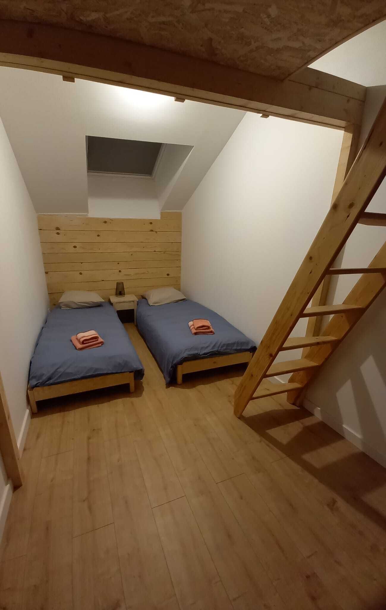 A small, narrow room with two wooden bunk beds, a sloped ceiling, and a wooden ladder.