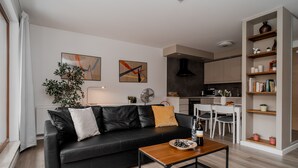 Ein modernes Wohnzimmer mit einer schwarzen Ledersofa, einem Holztisch und einem Essbereich mit weißem Tisch und Stühlen.