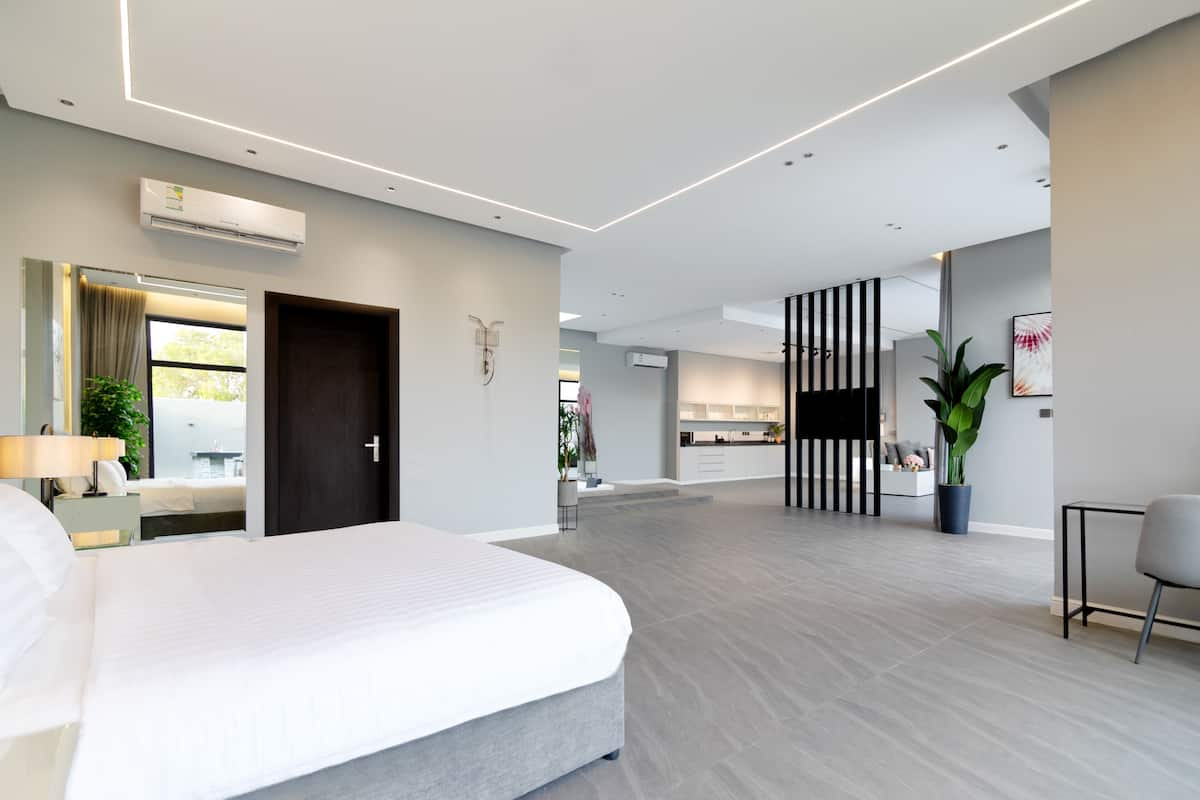 A modern hotel room with a large bed, a desk, and a kitchenette in the background.