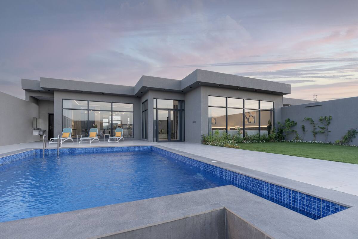 A modern house with a swimming pool, large windows, and a well-maintained lawn.