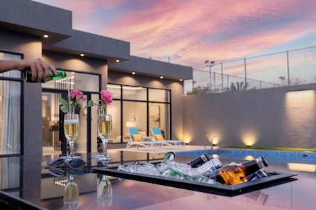 A bar area with a tray of ice, glasses, and bottles, overlooking a pool with lounge chairs.