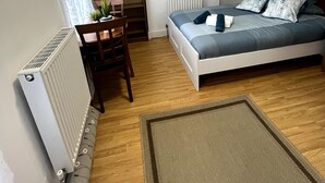 Ein Schlafzimmer mit Bett, Schreibtisch, Stuhl, Heizkörper und einem Fenster mit Vorhängen.