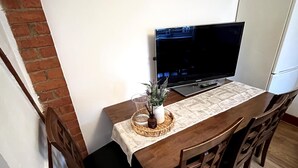 Ein Essbereich mit Holztisch, Stühlen, einem Fernseher und einem Kühlschrank.