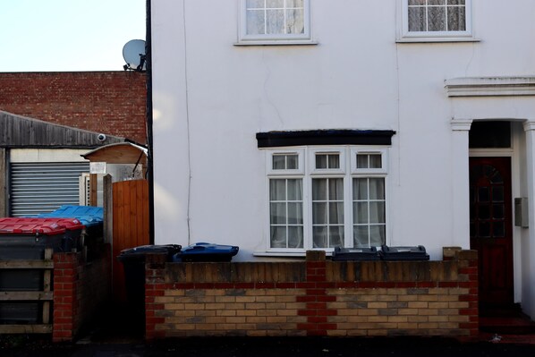 A white two-story house with a brick wall, a garage door, and a red door. - Cosy Entire 3-bed House With Garden and Fast Wifi (Croydon)