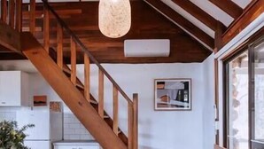 Ein geräumiger Raum mit einer Holztreppe, einem Essbereich mit Stühlen, einem Tisch und einer Pendelleuchte.
