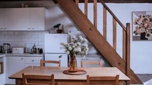 Eine Holztreppe führt zu einer Küche mit weißen Schränken, einem Esstisch mit Stühlen und einer hängenden Leuchte.