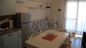 A compact kitchen with a microwave, refrigerator, and a dining area with a table and chairs. - Well-equipped 1 Bedroom Flat for up to 5 Guests (San Michele al Tagliamento)